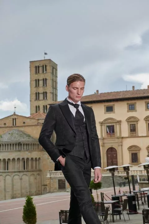 Abito elegante Rocchini 33 indossato da modello in piazza storica, sfondo di edifici antichi e cielo nuvoloso.