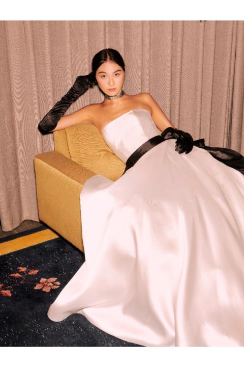 Abito da sposa Marilù Sposae Essential, elegante con guanti neri e cintura, su divano giallo.