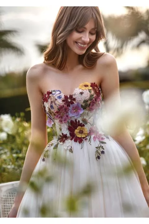 Abito da sposa AQUA con ricami floreali colorati su sfondo bianco, ambientato in un giardino.