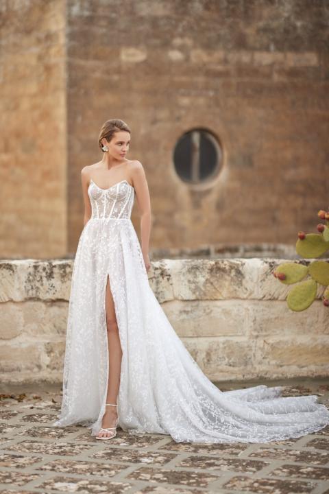 Abito da sposa AVENTURINE di Mark Loren, design elegante con spacco, sfondo architettura storica.