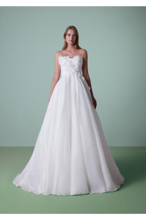 Abito da sposa DAULIS bianco senza spalline con dettagli floreali su sfondo verde.
