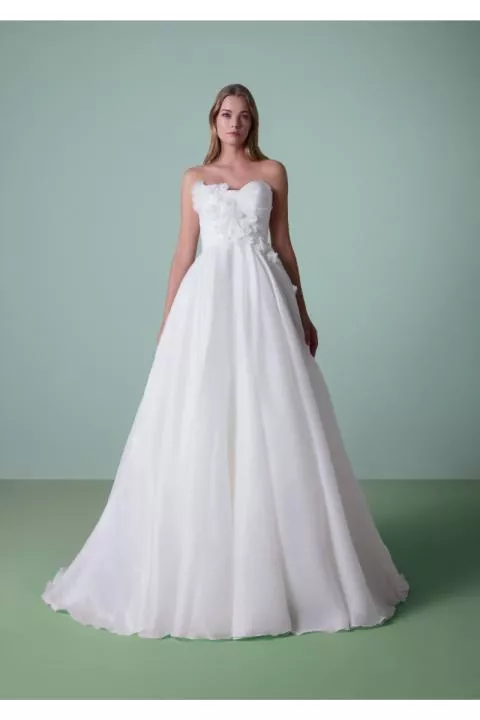 Abito da sposa DAULIS bianco senza spalline con dettagli floreali su sfondo verde.