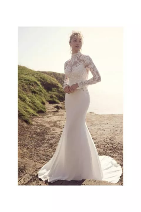 Abito da sposa Dionne Maggie Sottero con pizzo floreale e maniche lunghe, sfondo paesaggio costiero.