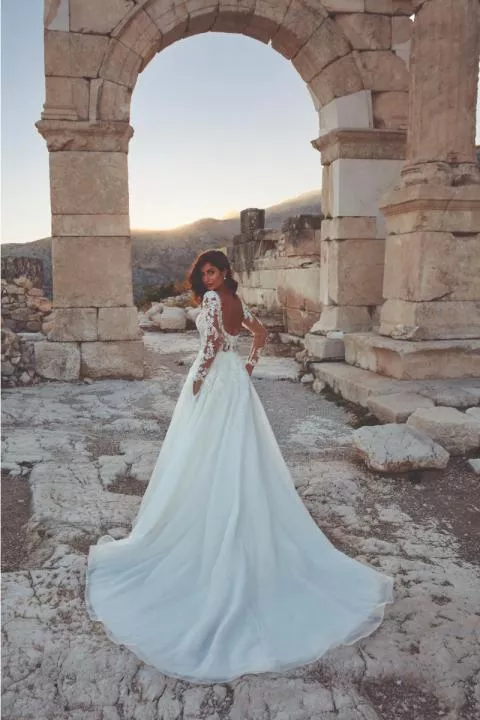 Abito da sposa Ireland Eddy K con dettagli in pizzo, sfondo di rovine antiche al tramonto.