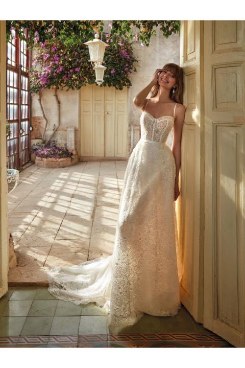 Abito da sposa EILA in pizzo bianco, ambientato in un cortile fiorito con luce naturale.