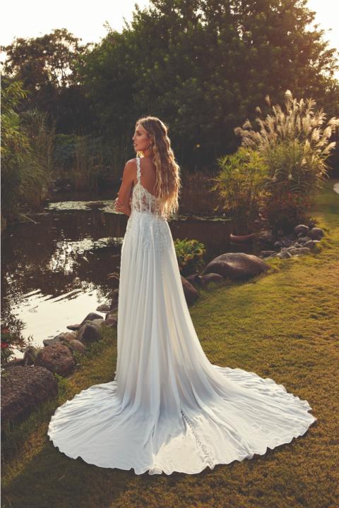 Abito da sposa ROSIE EDDY K con schiena scoperta, lungo strascico, in un giardino al tramonto.