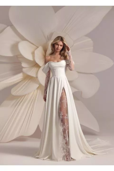 Abito da sposa BACCARA di Eva Lendel con spacco e dettagli in pizzo, sfondo floreale elegante.