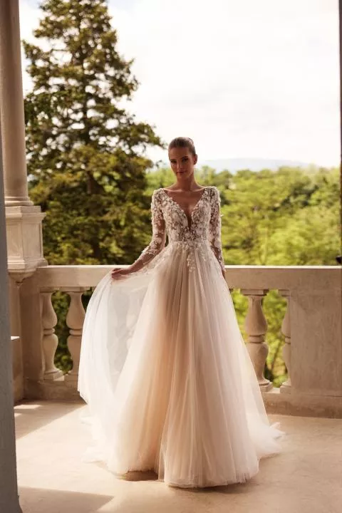 Abito da sposa Felicia Dama in pizzo floreale, maniche lunghe, sfondo verde naturale.