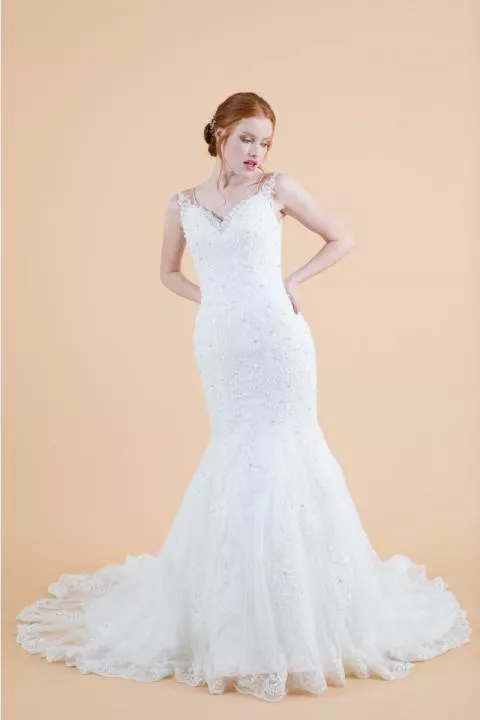 Abito da sposa Agatea in pizzo bianco con strascico, modello sirena, sfondo beige.
