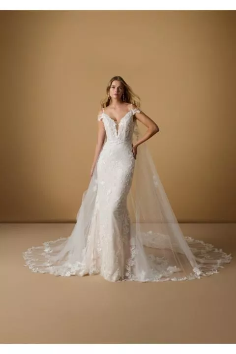Abito da sposa INGE in pizzo con strascico, spalline sottili, sfondo beige.