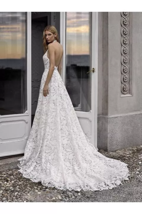 Abito da sposa Nicole Milano KIA in pizzo floreale, schiena scoperta, ambientazione elegante.