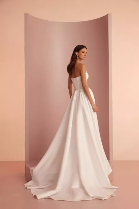 Abito da sposa elegante L411 ARIAMO LIGHT, schiena scoperta, lungo strascico, sfondo rosa.