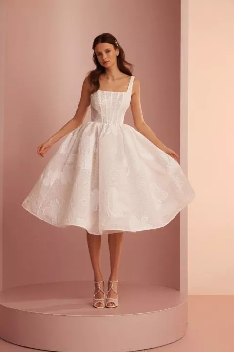 Abito bianco elegante L424 ARIAMO LIGHT con corpetto strutturato e gonna ampia, sfondo rosa.