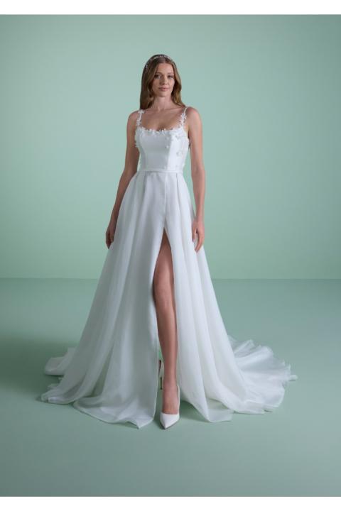 Abito da sposa MELAENA bianco con spacco e dettagli floreali, indossato da modella su sfondo verde.