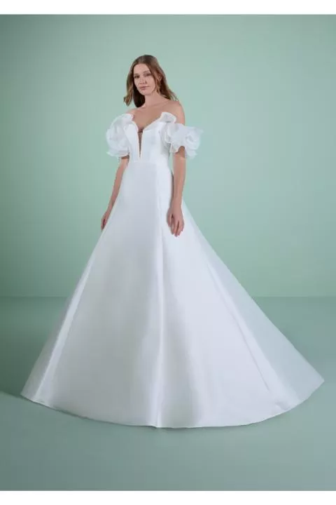 Abito da sposa MILOS bianco, scollo a cuore, maniche a sbuffo, fondo svasato, sfondo verde.