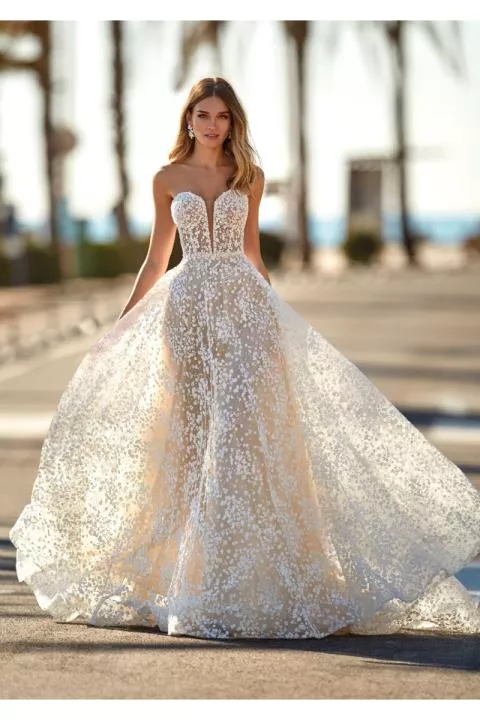 Abito da sposa MINDY con corpetto ricamato e gonna ampia, sfondo esterno con palme.