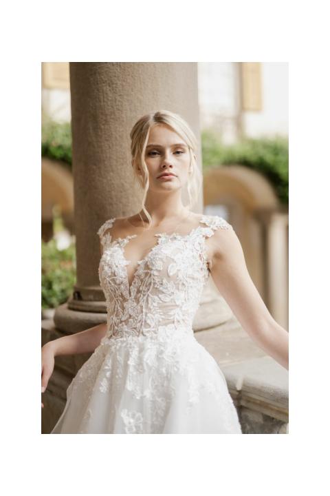 Abito da sposa IRIDE di Sposae Atelier con dettagli floreali, scollatura profonda e sfondo elegante.