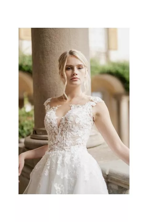 Abito da sposa IRIDE di Sposae Atelier con dettagli floreali, scollatura profonda e sfondo elegante.