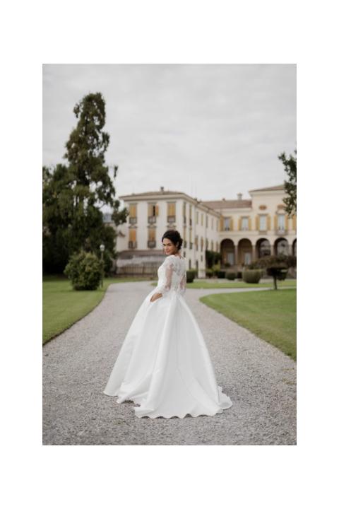 Abito da sposa ASTREO di Sposae Atelier, donna in giardino con edificio storico sullo sfondo.