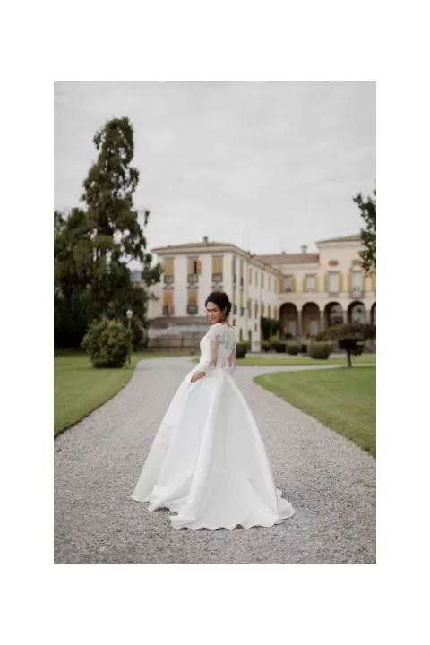 Abito da sposa ASTREO di Sposae Atelier, donna in giardino con edificio storico sullo sfondo.