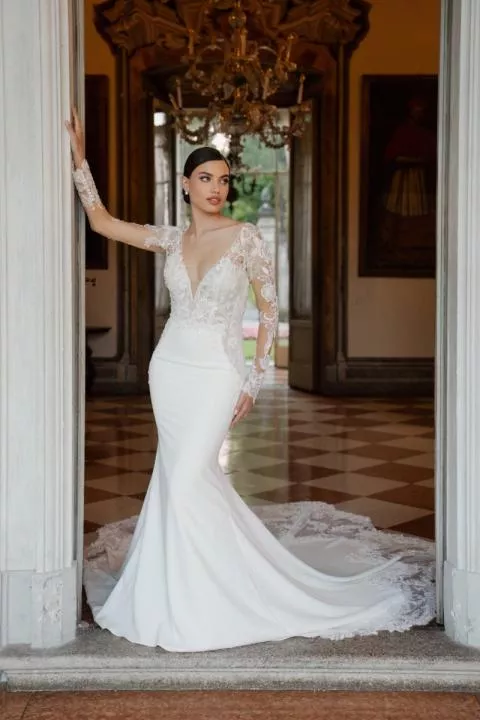 Abito da sposa KYLA in pizzo e seta, maniche lunghe, scollatura a V, ambientato in un elegante salone.