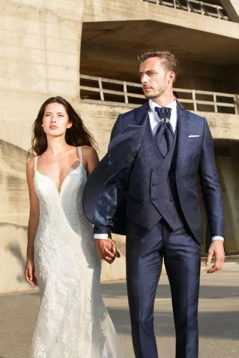 Coppia elegante in abiti da cerimonia, uomo in completo blu PALAZZO C8 158, donna in abito bianco, esterno.