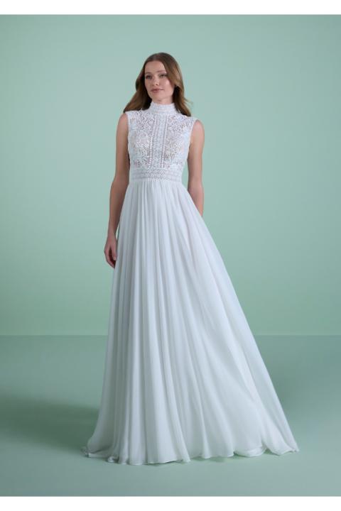 Abito da sposa PHIGALIA in pizzo bianco con gonna fluida, sfondo verde.