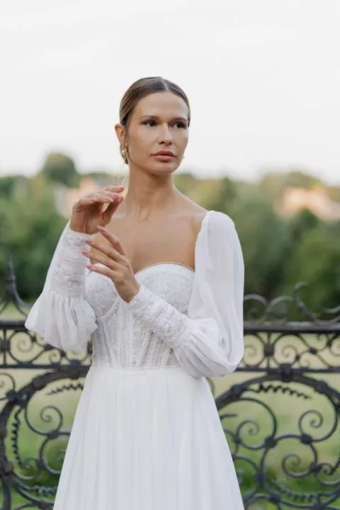 Abito da sposa Marlene con maniche lunghe, dettagli in pizzo, sfondo naturale.