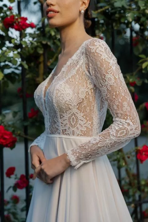 Abito da sposa in pizzo con maniche lunghe e scollo a V, circondato da rose rosse, modello JOAN di Romantica by Sposae.