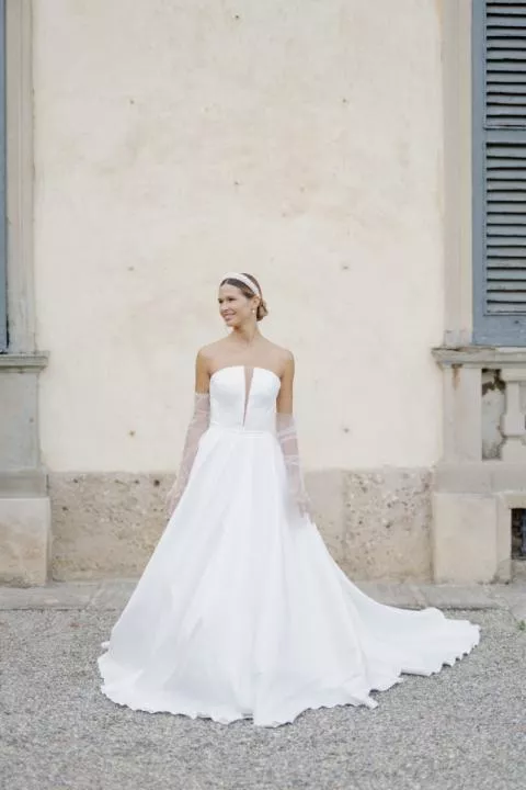 Abito da sposa bianco senza spalline, ESPERANCE di SPOSAE ATELIER, indossato da modella sorridente all'aperto.