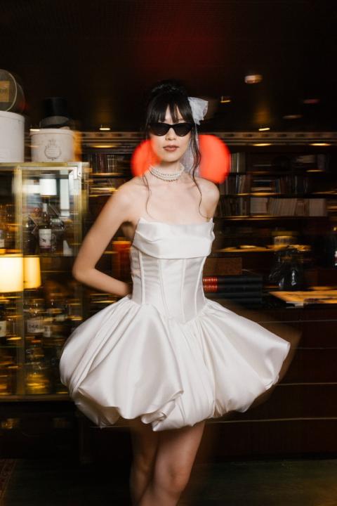 Abito da sposa corto MILANO - ESSENTIAL BY SPOSAE, stile moderno con occhiali da sole e collana di perle.