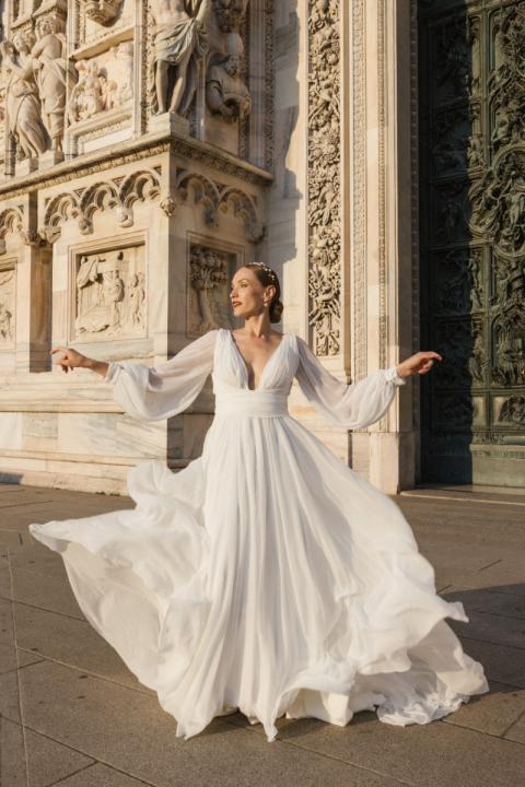 Abito da sposa ADELE 2.0 di Sposae, elegante e fluente, indossato davanti a un edificio storico.