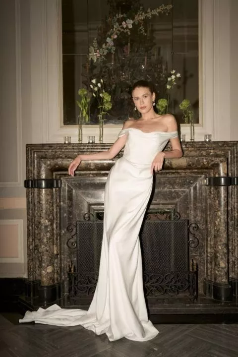 Abito da sposa bianco elegante Vivienne, collezione The Romantica, su modella davanti a caminetto decorato.