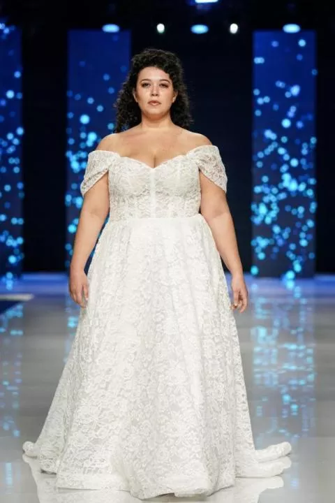 Abito da sposa curvy in pizzo bianco, scollo a cuore, sfilata moda.