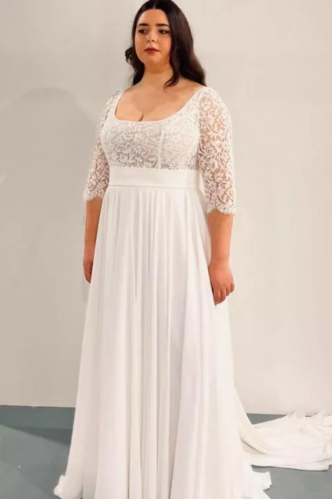 Abito da sposa curvy Carmen con corpetto in pizzo e maniche a tre quarti, gonna fluida bianca.