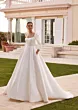 Abito da sposa Bertha in raso bianco con maniche lunghe, scollo quadrato, ambientato in giardino elegante.