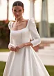 Abito da sposa Bertha con scollo quadrato e maniche lunghe in stile elegante, sfondo esterno sfocato.