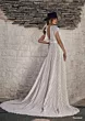 Abito da sposa boho Moondust di Ariamo, pizzo bianco, schiena scoperta, cappello nero, sfondo muro in pietra.