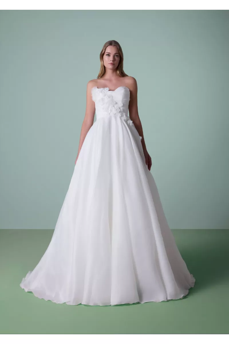 Abito da sposa DAULIS bianco senza spalline con dettagli floreali su sfondo verde.