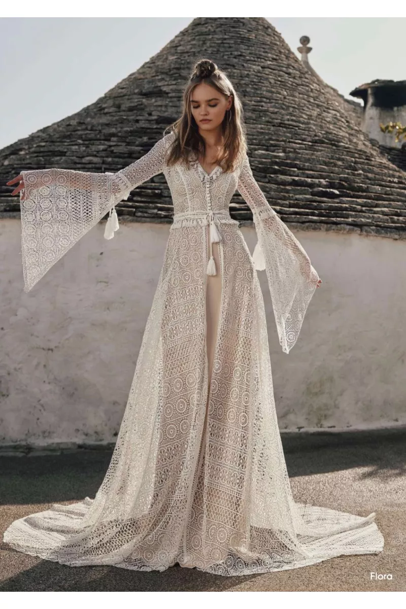 Abito boho in pizzo bianco con maniche ampie, sfondo architettura tradizionale.
