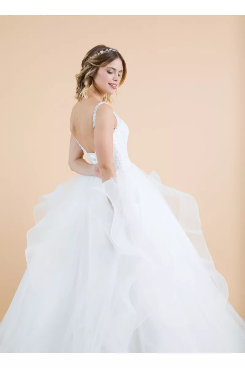 Abito da sposa Biancospino in tulle bianco con spalline sottili e dettagli floreali, sfondo beige.