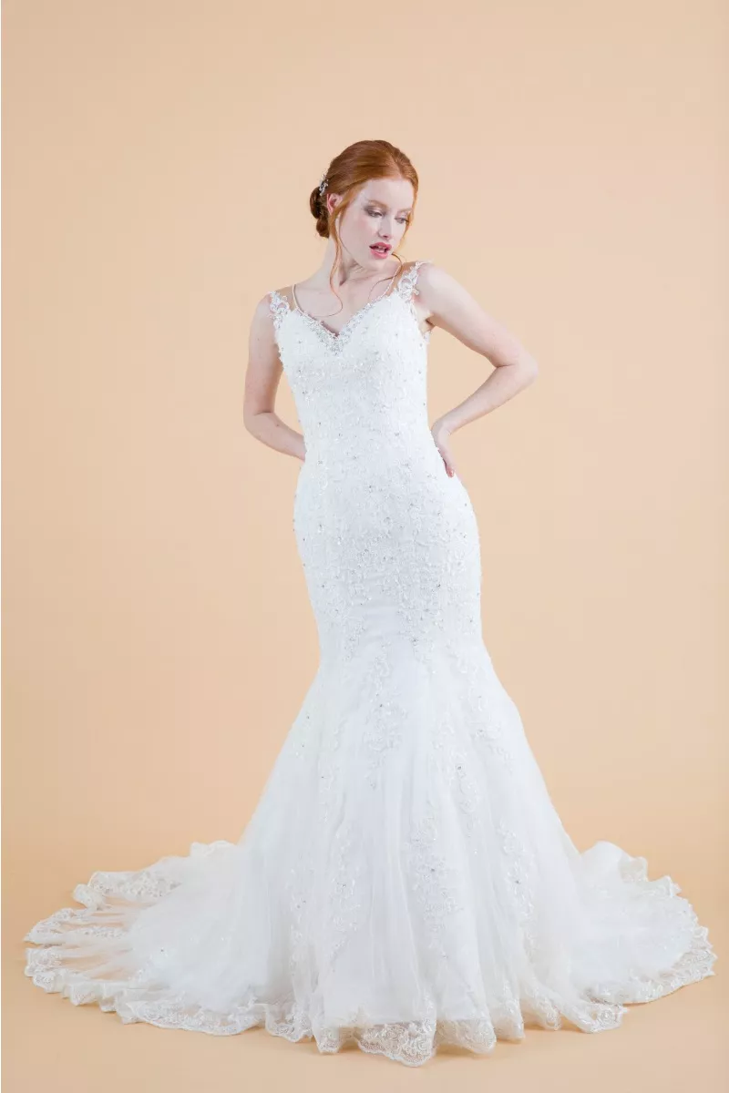 Abito da sposa Agatea in pizzo bianco con strascico, modello sirena, sfondo beige.