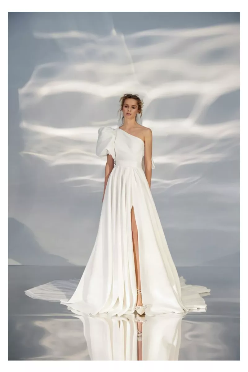 Abito da sposa bianco monospalla con spacco, modello L320 Ariamo Light, sfondo effetto onde di luce.