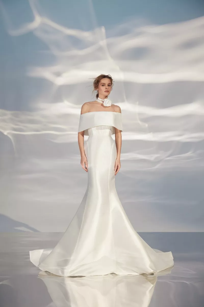 Abito da sposa bianco ARIAMO LIGHT L321 con scollo a barca e decorazione floreale, sfondo celeste.