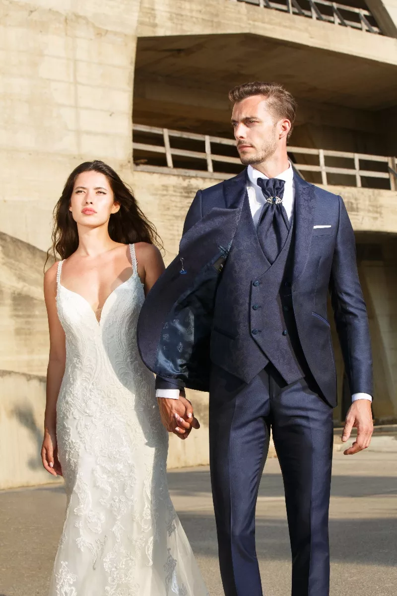 Coppia elegante in abiti da cerimonia, uomo in completo blu PALAZZO C8 158, donna in abito bianco, esterno.