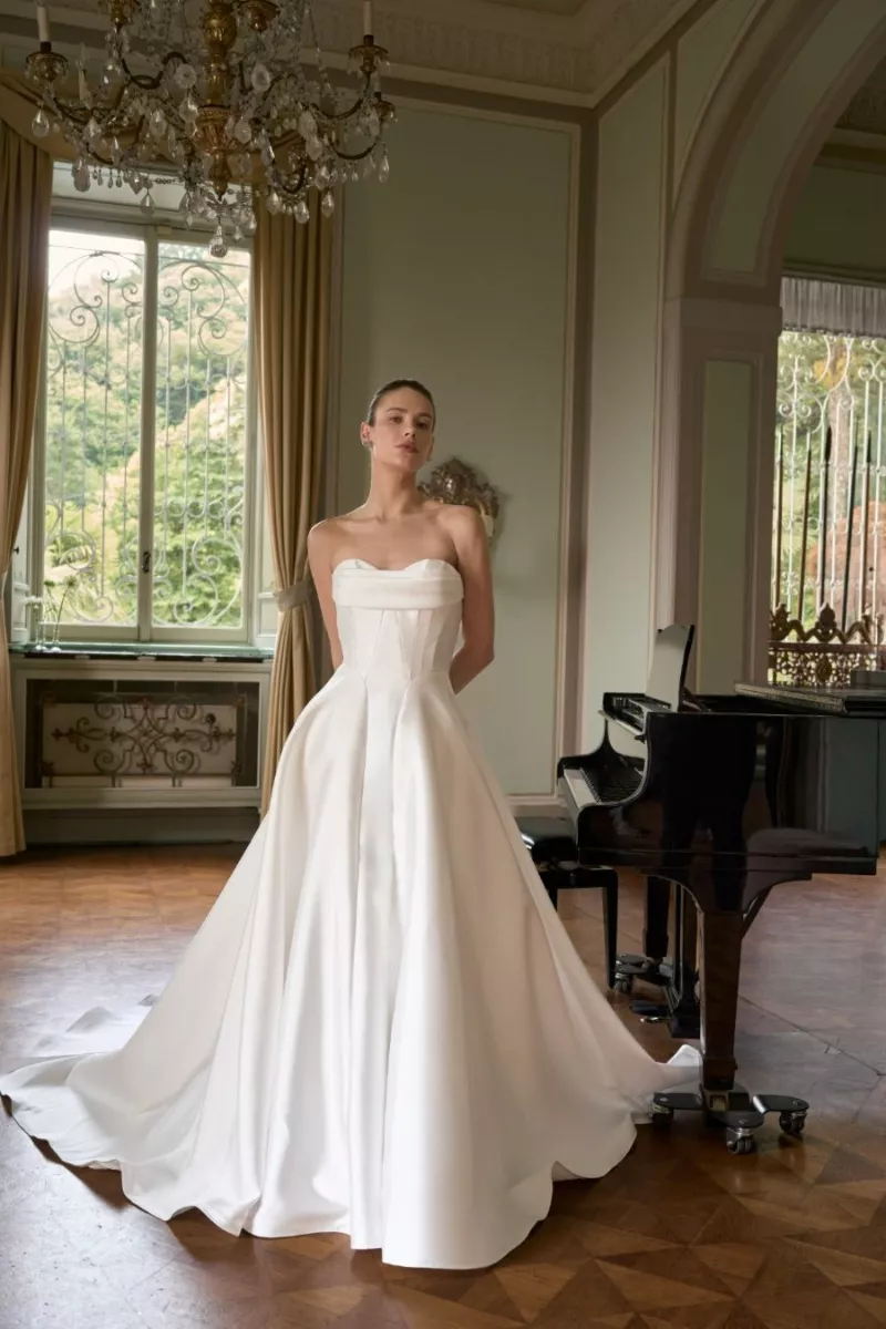 Abito da sposa elegante MILA, The Romantica Collection, in salone classico con pianoforte e lampadario.