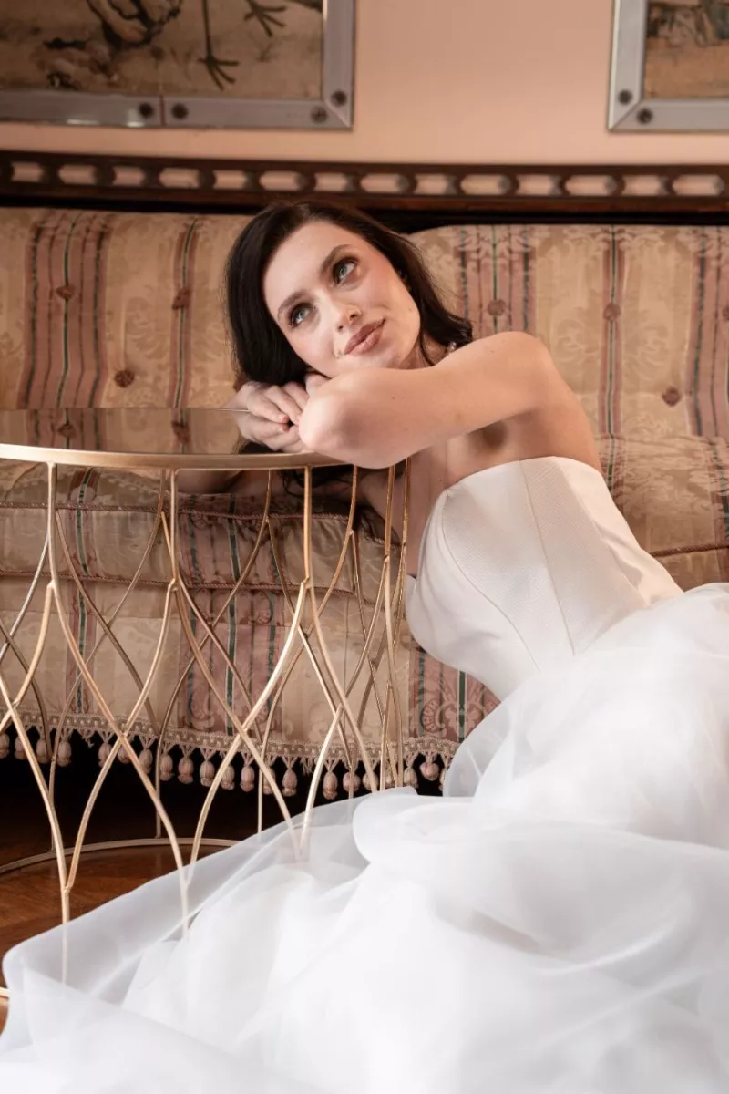 Abito da sposa elegante DARIA, collezione Romantica, donna sognante su divano vintage e tavolino dorato.