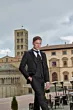 Abito elegante Rocchini 33 indossato da modello in piazza storica, sfondo di edifici antichi e cielo nuvoloso.