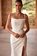 Abito elegante bianco Charmony Dama con spalline sottili e spacco, indossato da modella in ambiente esterno.