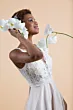 Abito da sposa girasole in pizzo bianco con dettagli floreali, donna sorridente con orchidee bianche.
